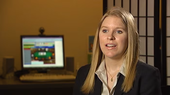 Foto de una autora rubia con chaqueta oscura, sentada en una oficina delante de una pantalla de ordenador